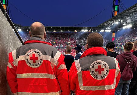 Sanitätsdienst Stadion UEFA EM 2 Sanitäter stehen mit dem Rücken zur Kamera und schauen auf das Spielfeld des Rhein Energie Stadions in Köln durch ein Mundloch im Oberrang